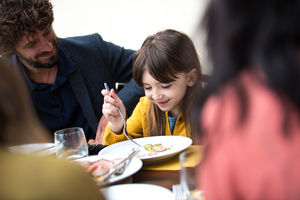 Father smiling at daughter eating meal