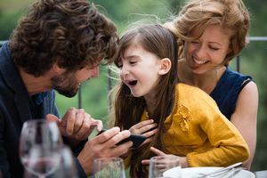 Family laughing with smartphone outdoors