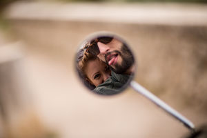 Reflection in motorbike mirror of couple fooling around