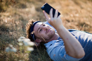 Young adult lying on grass in summer using smartphone