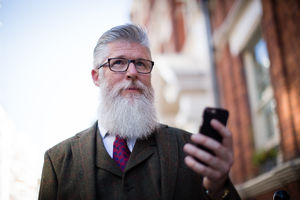 Senior male walking down street using smartphone