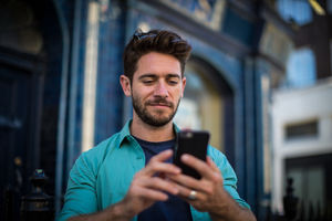 Young adult standing outside London pub using smartphone