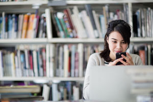 Student using smartphone and laptop in library