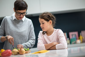 Mum teaching daughter to chop vegetables