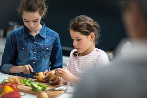 Mum watching daughters chop vegetables