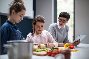 Mum teaching daughters a recipe using a digital tablet
