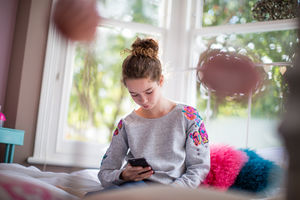 Teenager in bedroom looking at smartphone