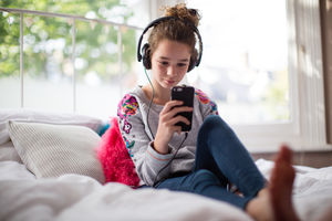 Teenager in bedroom listening to music on smartphone