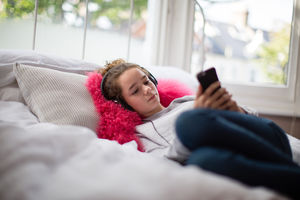 Teenager in bedroom listening to music on smartphone