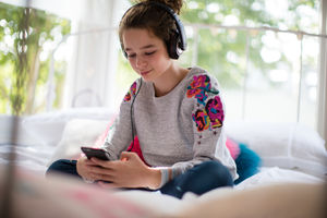 Teenager in bedroom listening to music on smartphone