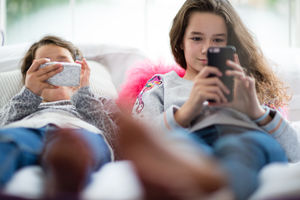 Sisters using smartphones in bedroom