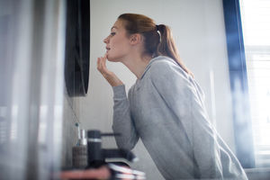 Young adult female putting looking at reflection in bathroom mirror