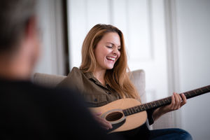 Young adult female playing acoustic guitar to friend