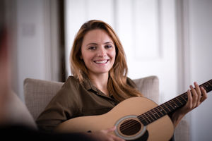 Young adult female playing acoustic guitar to friend