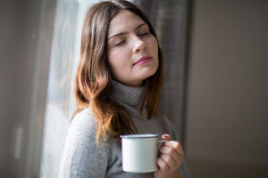 Young adult female leaning on window with mug in hand