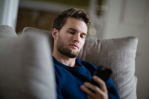 Young adult male using smartphone on sofa