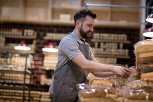 Baker in bakery stocking shelves and looking to camera