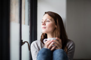 Young adult female having morning coffee and looking out of window