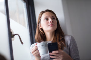 Young adult female having morning coffee and checking smartphone