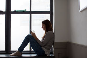 Young adult female sitting on window ledge with smartphone
