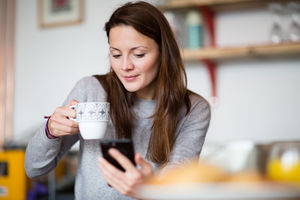 Young adult female having morning coffee and checking smartphone