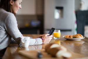 Young adult female having morning coffee and checking smartphone