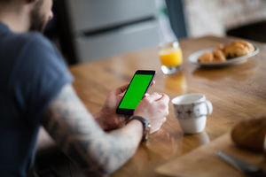 Young adult male having morning coffee and checking smartphone