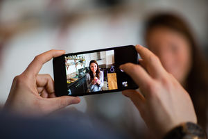 Smartphone taking photo of woman holding cupcake with candle