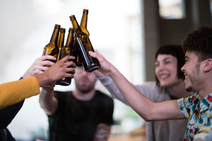 Group of friends clinking beer bottles at a house party