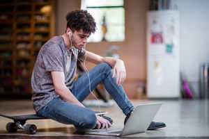 Young adult male sitting on skateboard using laptop