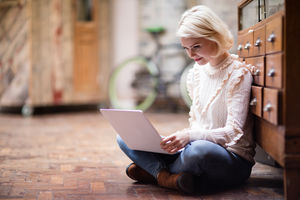 Young adult female sitting on floor working on laptop