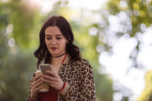 Trendy young adult female using smartphone in park in summertime