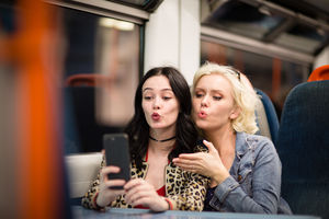 Young adult female friends travelling on a night train taking selfie