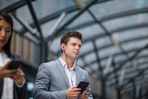 Businessman listening to podcast waiting for train at station