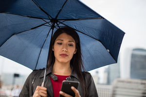 Businesswoman in city holding umbrella looking at smartphone