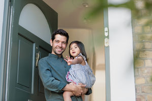 Father standing in home doorway with daughter waving