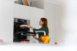 Adult female putting dish in oven