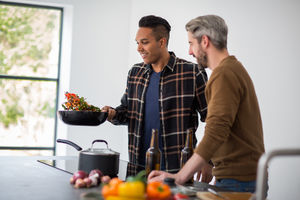 Male friends having a beer whilst cooking a stir fry