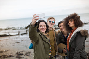 Group of young adult friends taking a selfie on a beach in winter