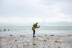 Young male skimming stones on a beach in winter