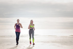 Active senior woman running with daughter on beach