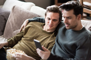 Young male couple relaxing on sofa streaming entertainment