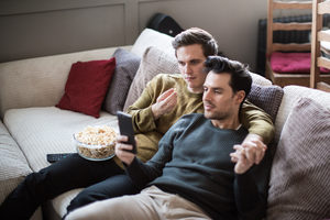 Young male couple relaxing on sofa streaming entertainment