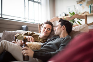 Young male couple relaxing on sofa with beer and popcorn