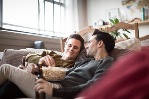 Young male couple relaxing on sofa with beer and popcorn