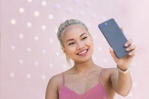 Young adult female taking selfie with pink background