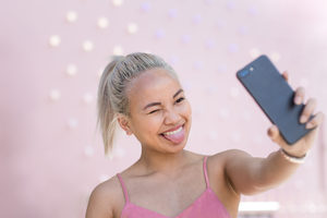 Young adult female taking selfie with pink background