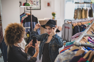 Millennial trying on a hat in a vintage clothing store