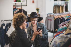 Millennial female friends looking at a smartphone in a vintage clothing store