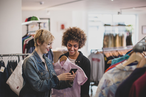 Millennial female friends looking at a smartphone in a vintage clothing store